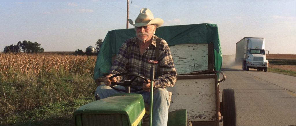 Alvin Straight (Richard Farnsworth) drives his riding lawnmower down the highway. A semi-trick prepares to pass him on the right