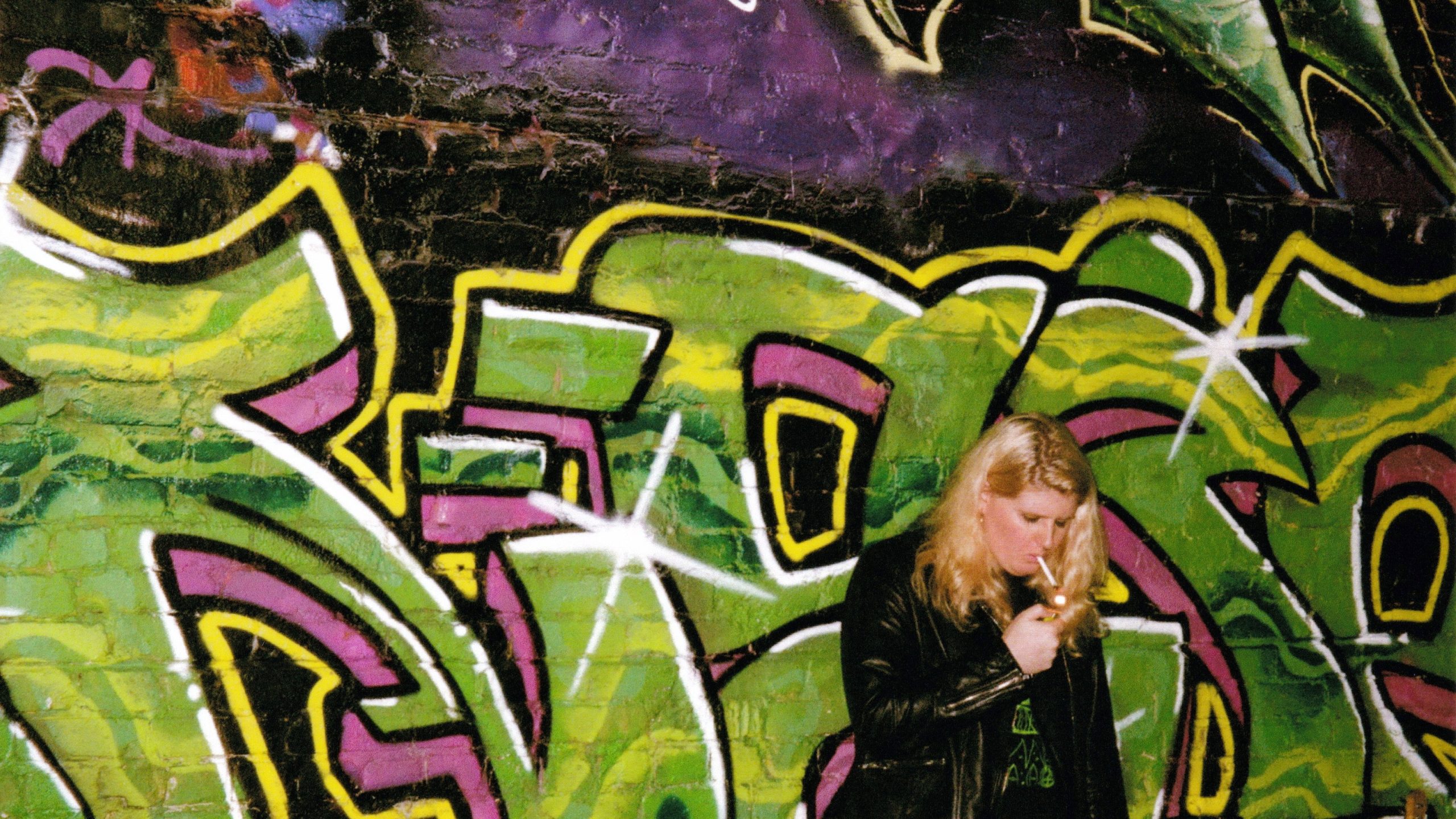 Traps rips a cigarette in front of a graffiti'd wall.
